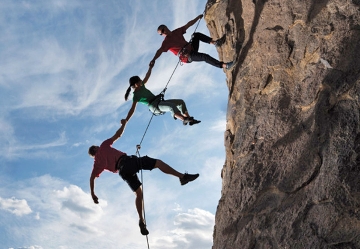 Silhouette of three people rock climbing