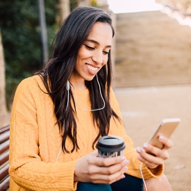 Young woman drinking coffee and listening to something on her phone