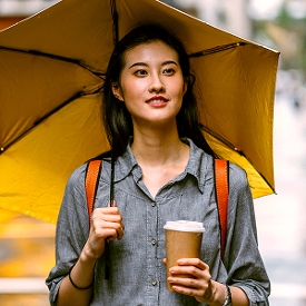 Young female walking with umbrella and coffee
